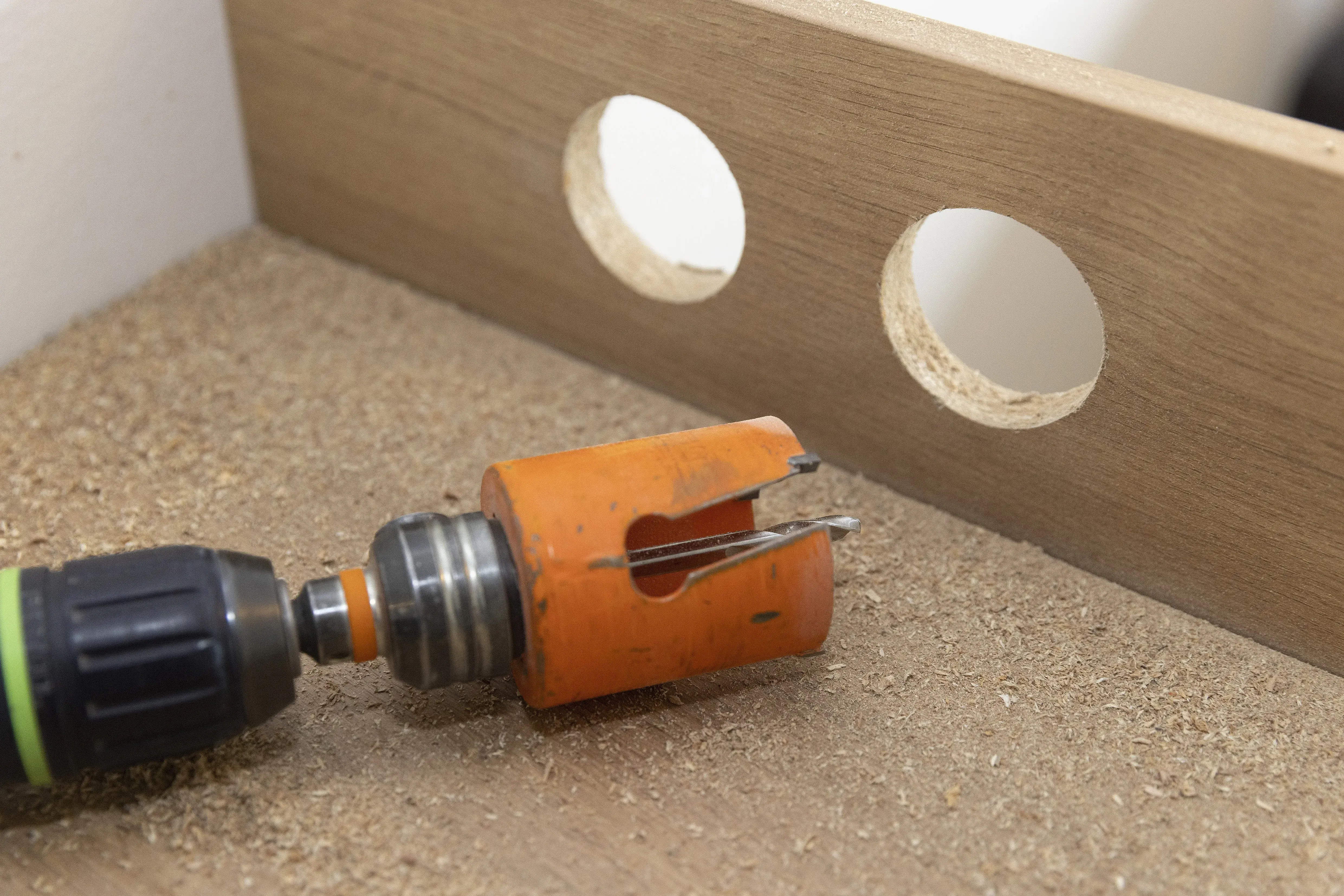Bohrmaschine mit Lochsäge neben Holz mit zwei gebohrten Löchern